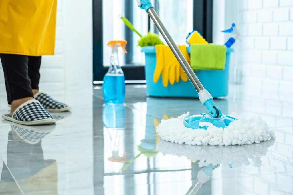 Cleaner mopping a polished tile floor beside a blue bucket of supplies